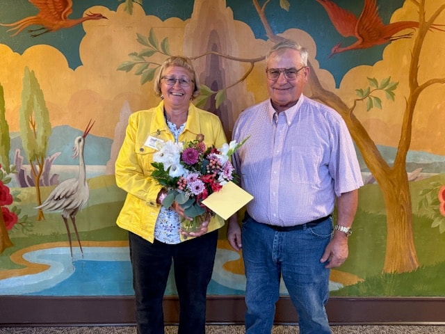 Annual meeting honoree holding a bouquet beside a colorful mural