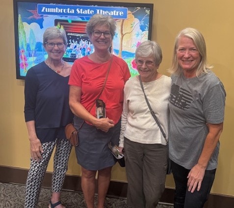 Four women posing in front of a Zumbrota State Theatre display