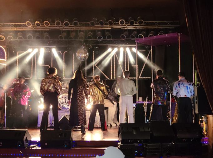 Disco performers on stage beneath bright concert lights