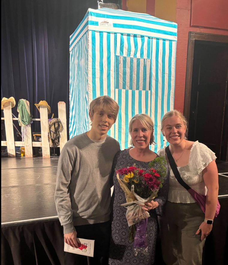 Three people posing with flowers beside a striped stage set