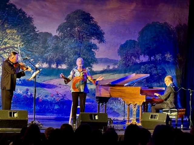 Violin, vocalist and piano trio performing before the painted stage backdrop