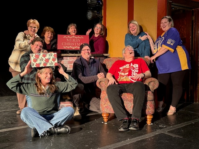 Holiday cast gathered around a chair on the theatre stage