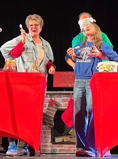 Two performers presenting behind bright red tables on stage